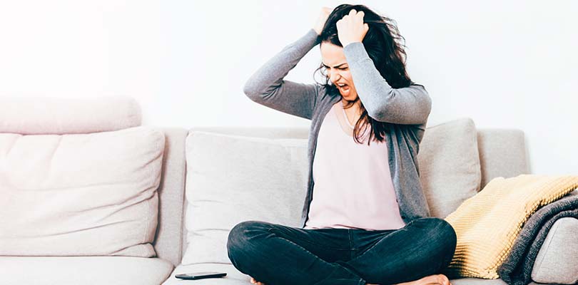 A woman sitting on a couch with her hands in her hair.