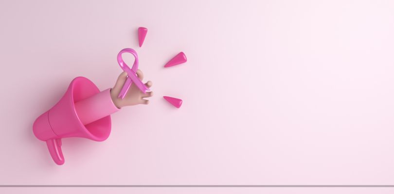 A pink megaphone with a hand coming out of it holding a breast cancer ribbon, on a pink background.