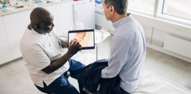 A man talking to his doctor, who is showing him an image of prostate cancer on a tablet screen.