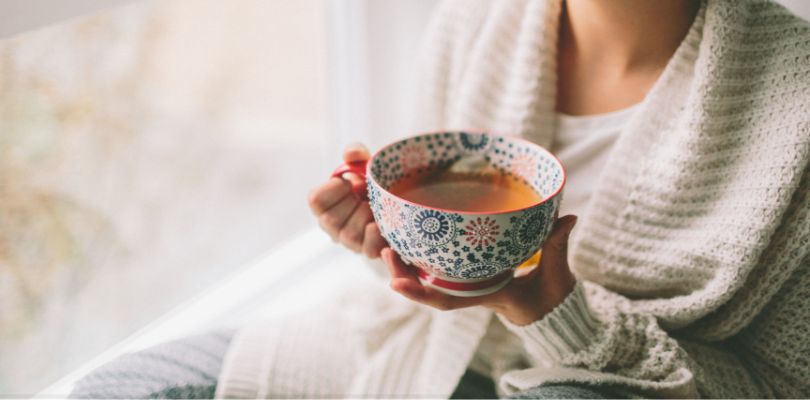 A woman holding a large cup of tea. She is wearing a white sweater.