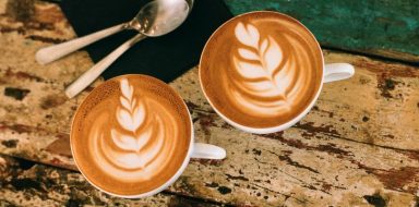 A top down view of two lattes on a wooden table.